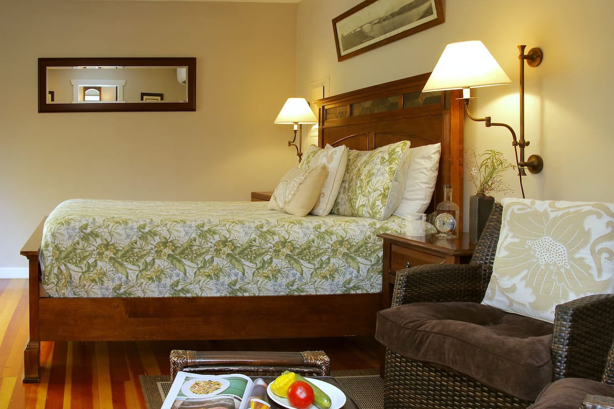 A hotel room with a bed, two chairs, a table with fruit, and wall-mounted lamps.