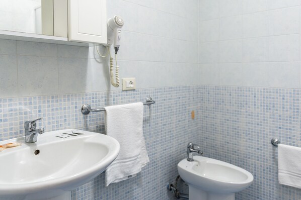 Une salle de bain équipée d’un lavabo, d’un bidet et d’un sèche-cheveux fixé au mur.