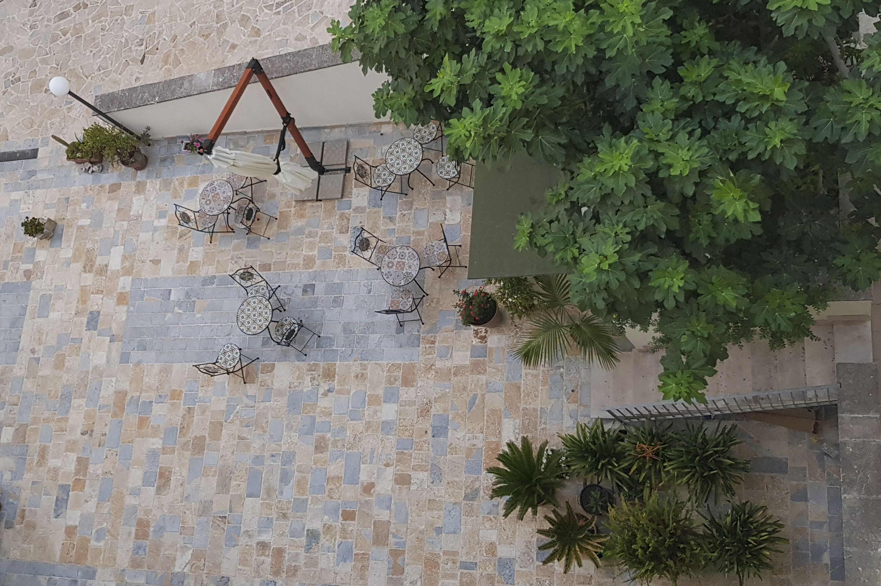 An outdoor patio with tiled flooring, multiple round tables with chairs, and potted plants.