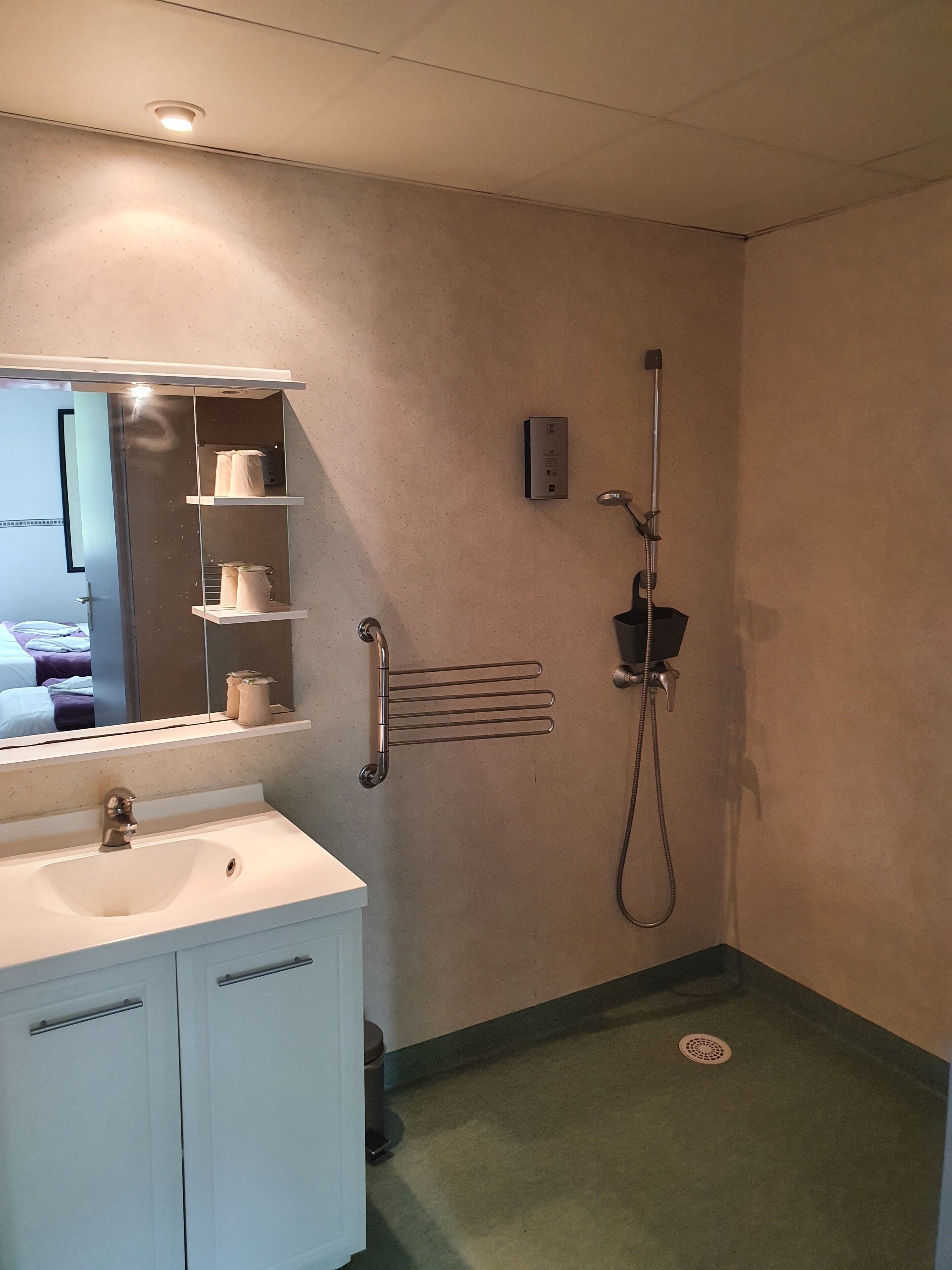Un baño con lavamanos blanco, espejo, toallero, ducha e inodoro.