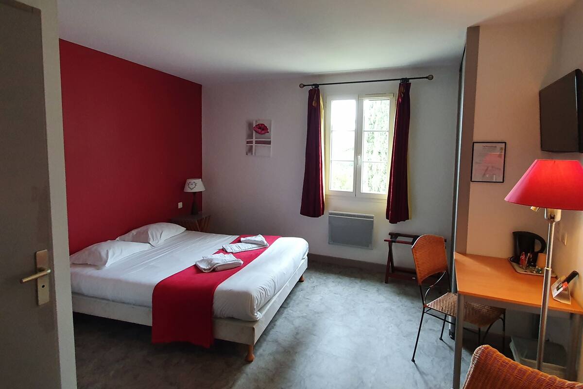 A hotel room with a bed, a desk, a chair, a window with curtains, a radiator, and a television.