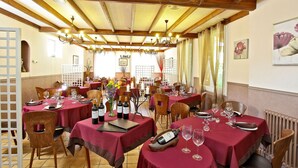 Un espace repas avec des tables rondes recouvertes de nappes rouges, des chaises en bois et des bouteilles de vin.