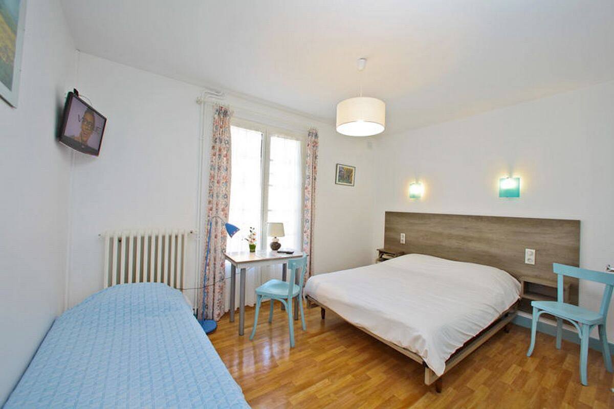 Een slaapkamer met een houten bed, een bureau met stoel, een radiator en een raam met gordijnen.