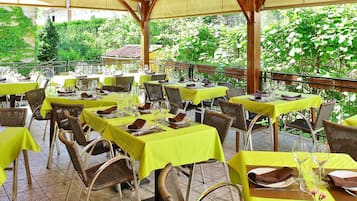 An outdoor dining area with tables and wicker chairs, surrounded by greenery.