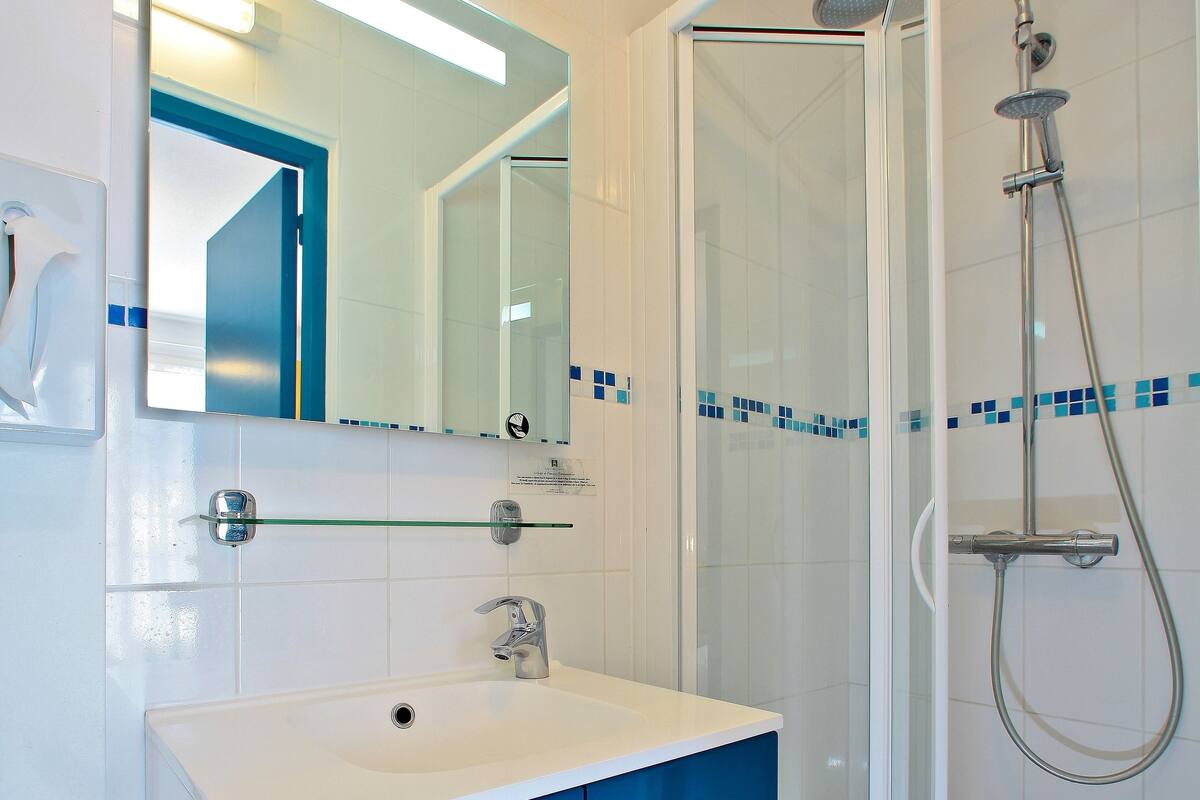 Een moderne badkamer met een witte wastafel, blauwe kastjes, een glazen douchecabine en een spiegel met een blauwe lijst.