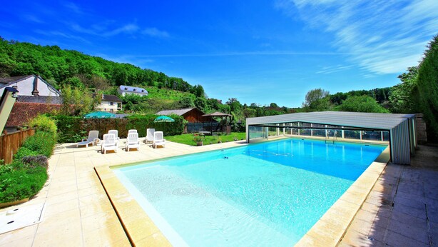 Une piscine rectangulaire avec une terrasse carrelée, entourée d’une clôture en bois et d’une pelouse.