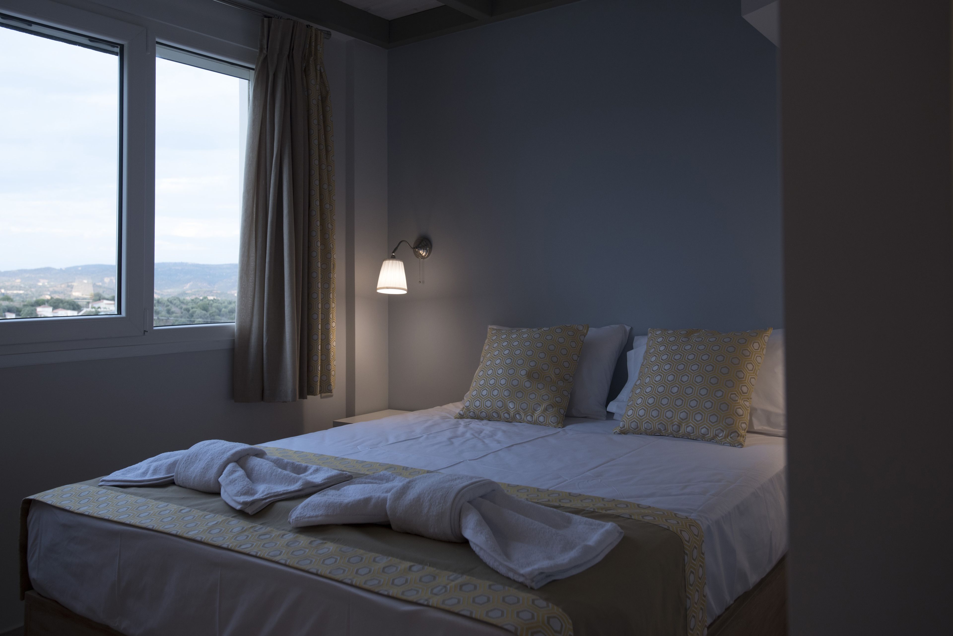 A hotel room with a bed, a window, and a wall-mounted lamp.