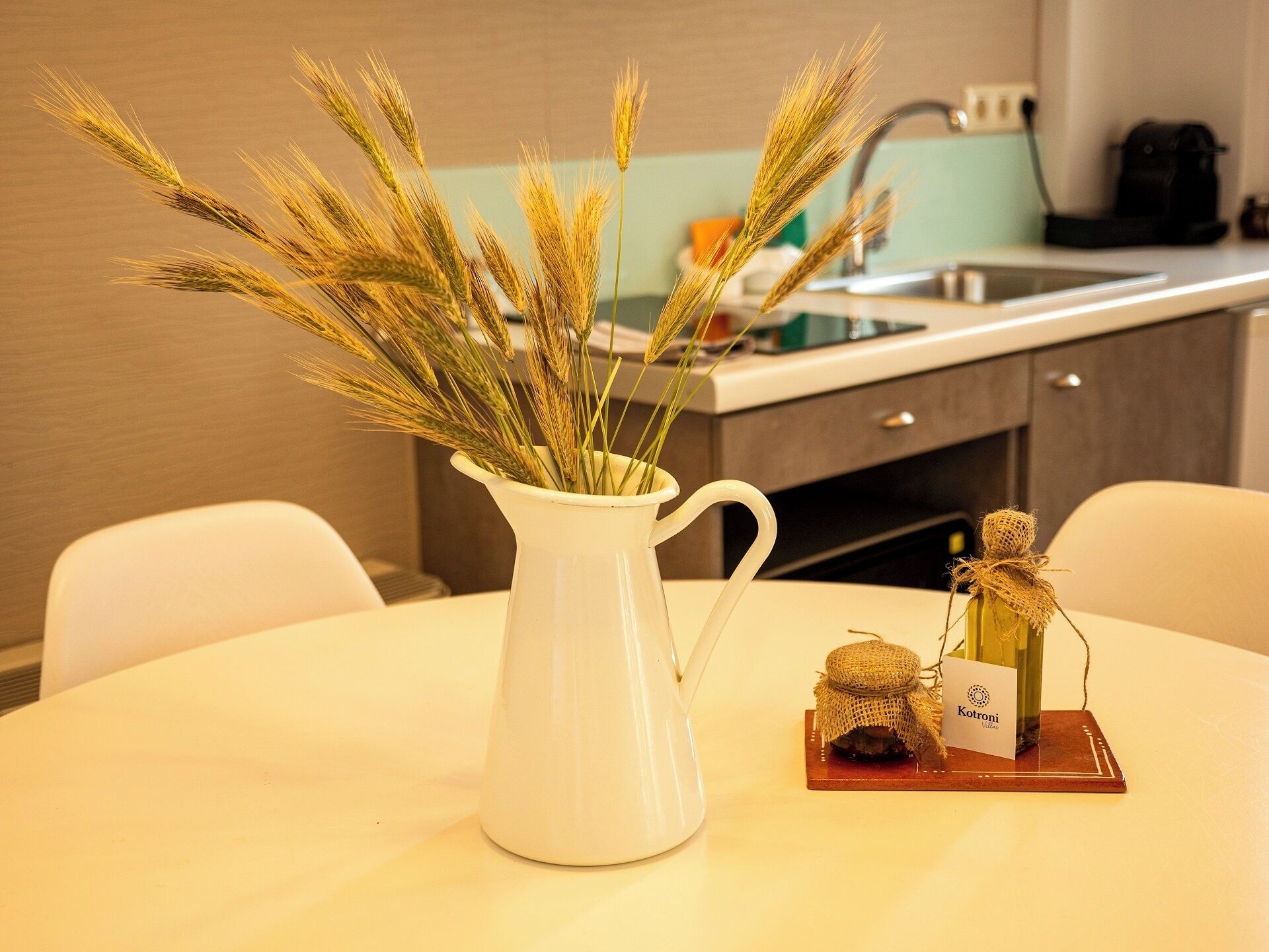 A white ceramic pitcher with wheat stalks on a round table in a modern kitchen with a sink and cabinets.