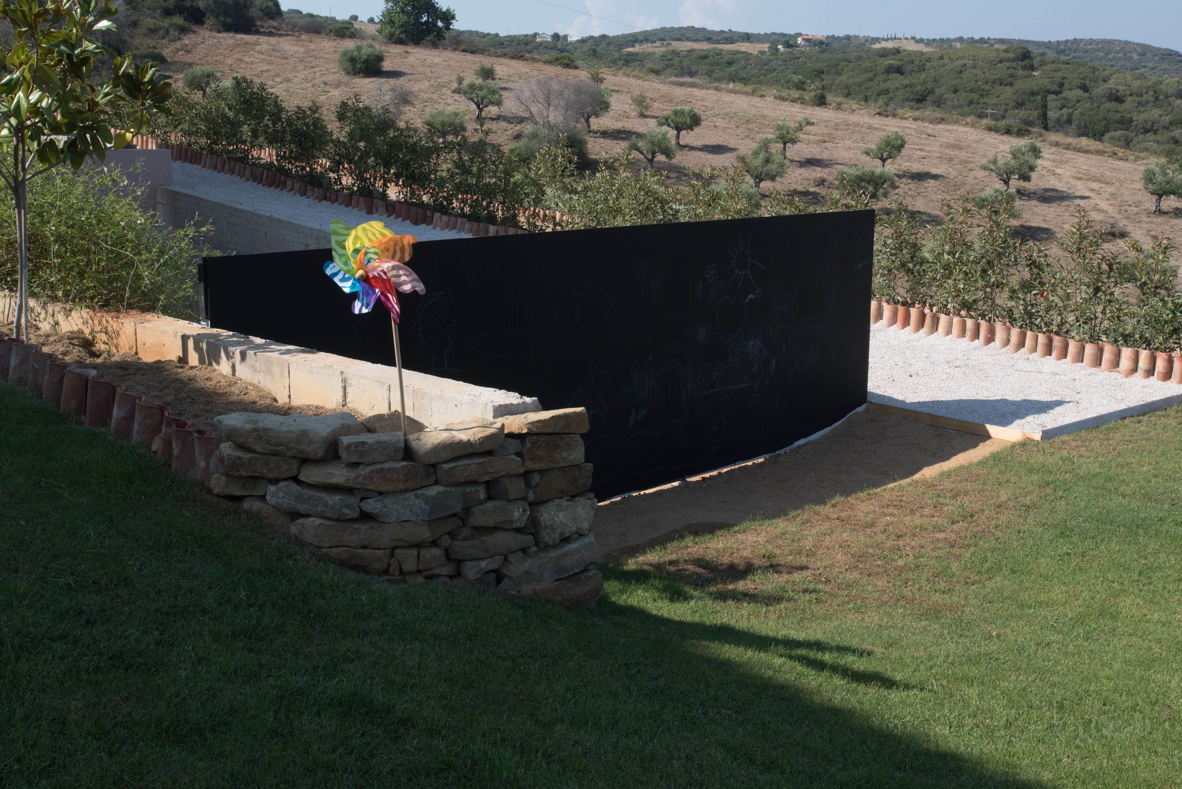 Un muro de piedra con una estructura negra, un área con césped y un paisaje montañoso al fondo.