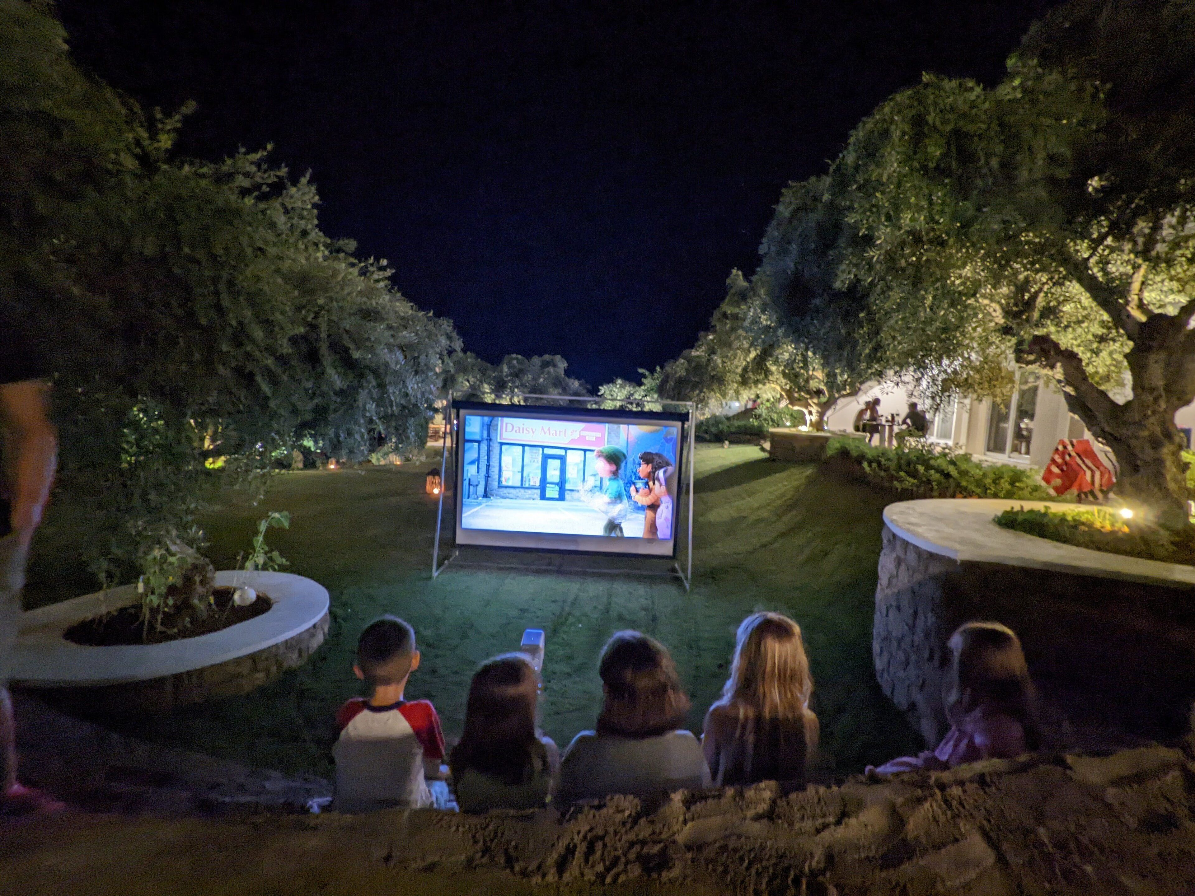 Tela de cinema ao ar livre com pessoas sentadas em frente.
