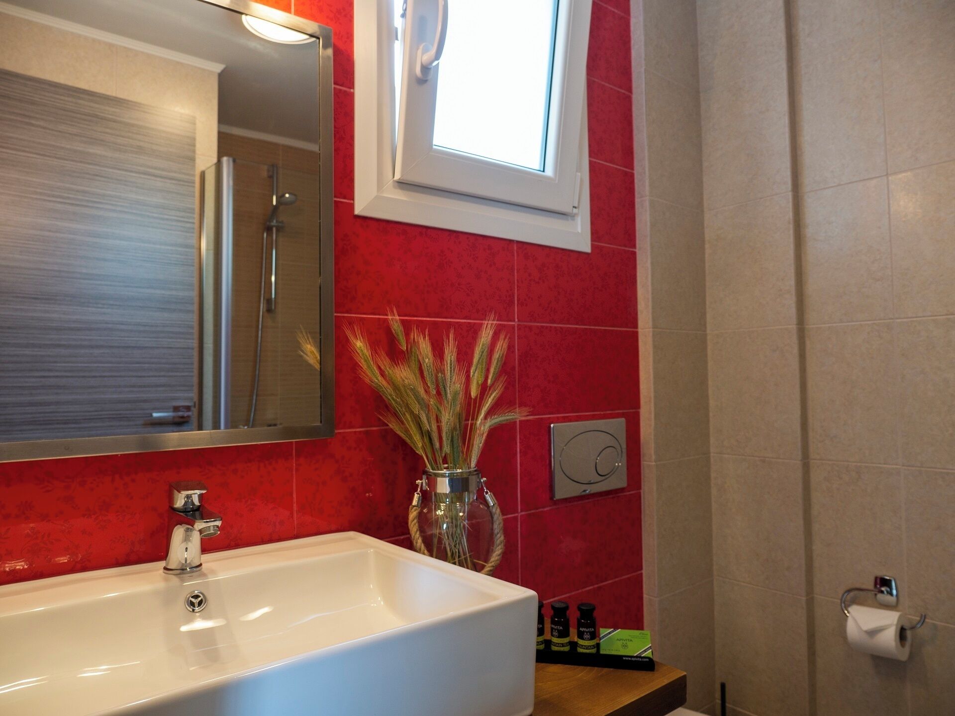 A bathroom with a white sink, a mirror, a window, and a red tiled wall.