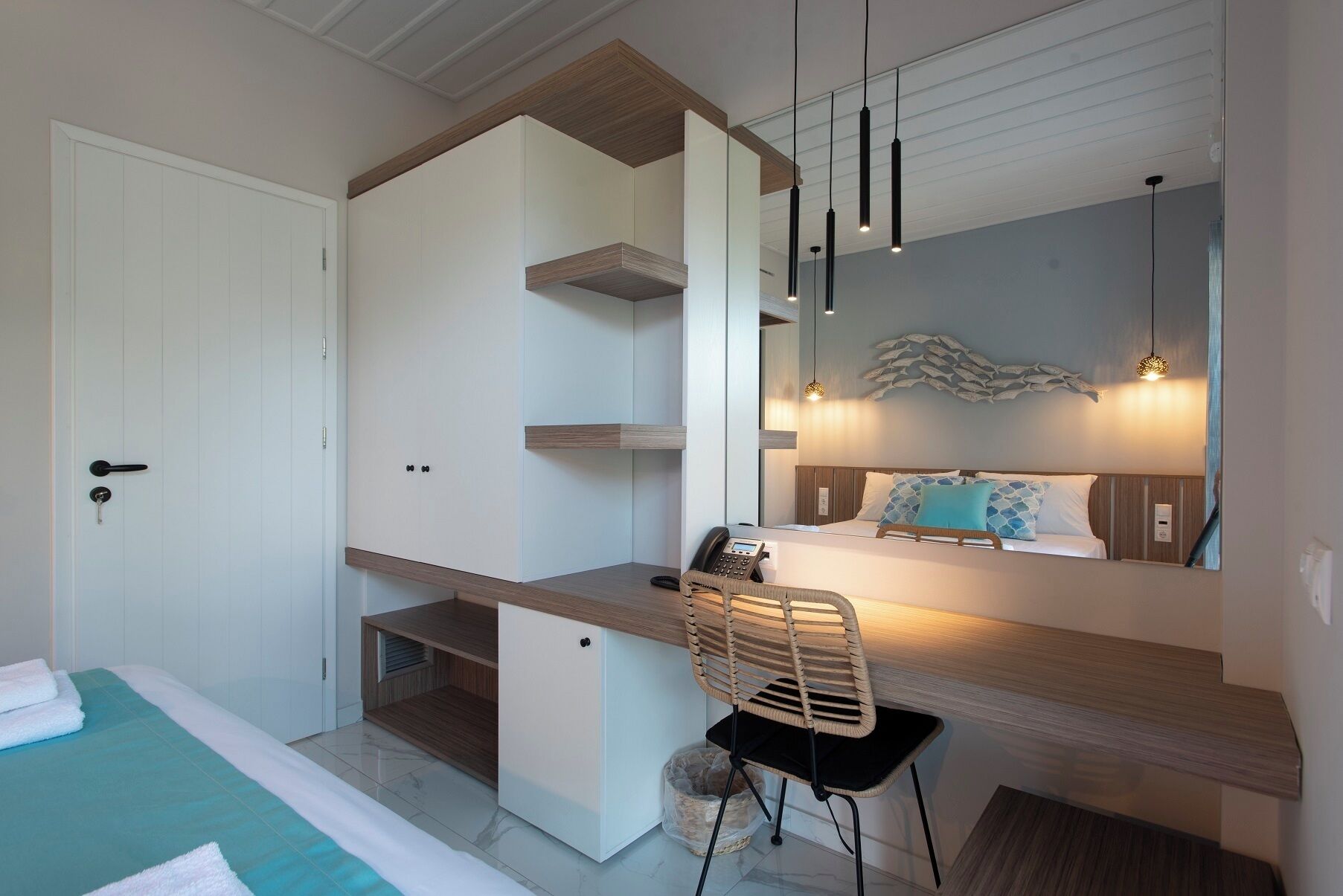 A modern bedroom with a bed, a desk, and a chair. There is a wardrobe with a mirror above the bed.