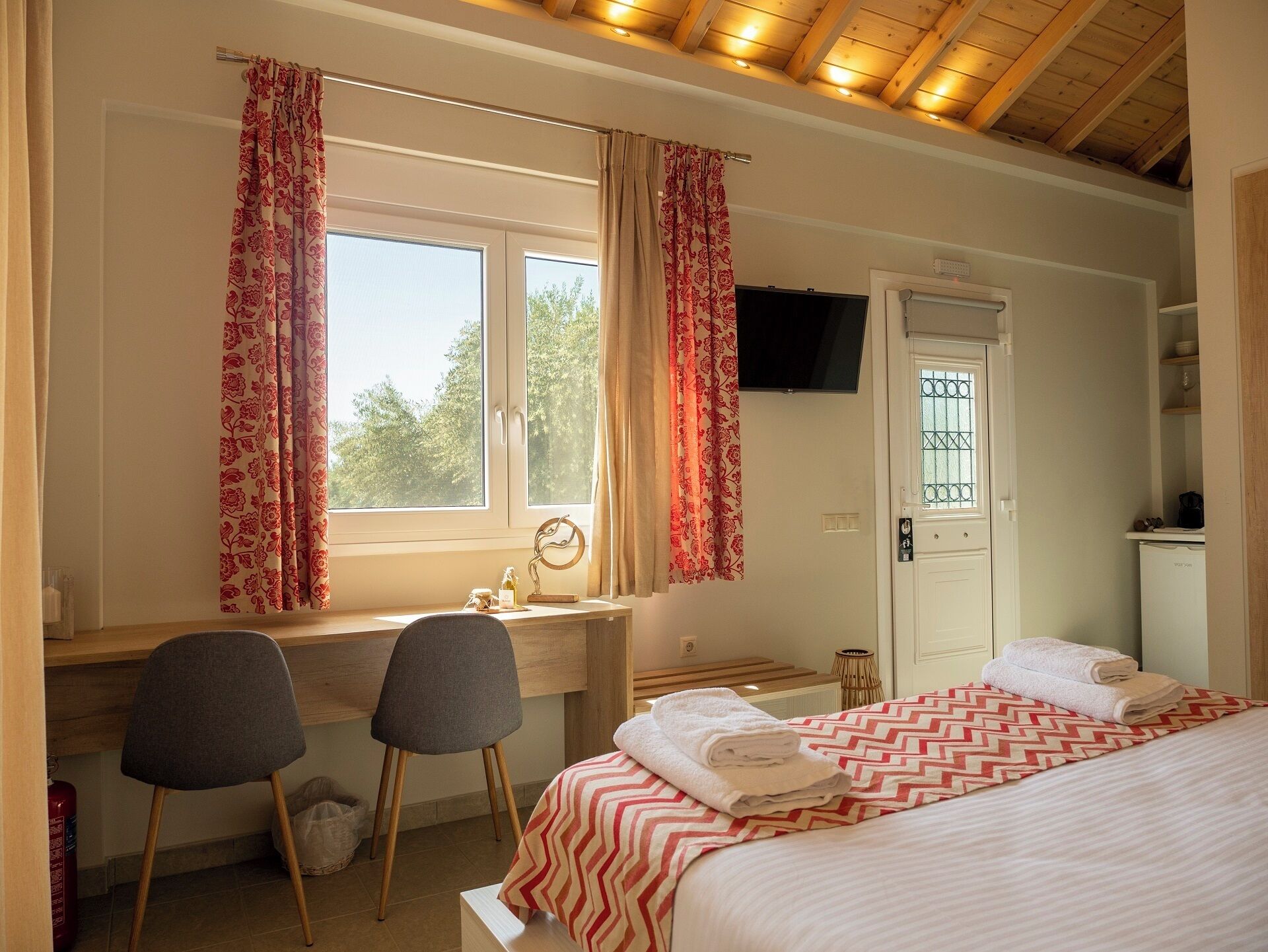 A bedroom with a bed, two chairs, a desk, a TV, and a door with a window.