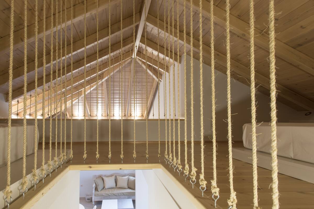 Quarto no estilo loft com teto inclinado, vigas de madeira e uma instalação de balanço em corda.