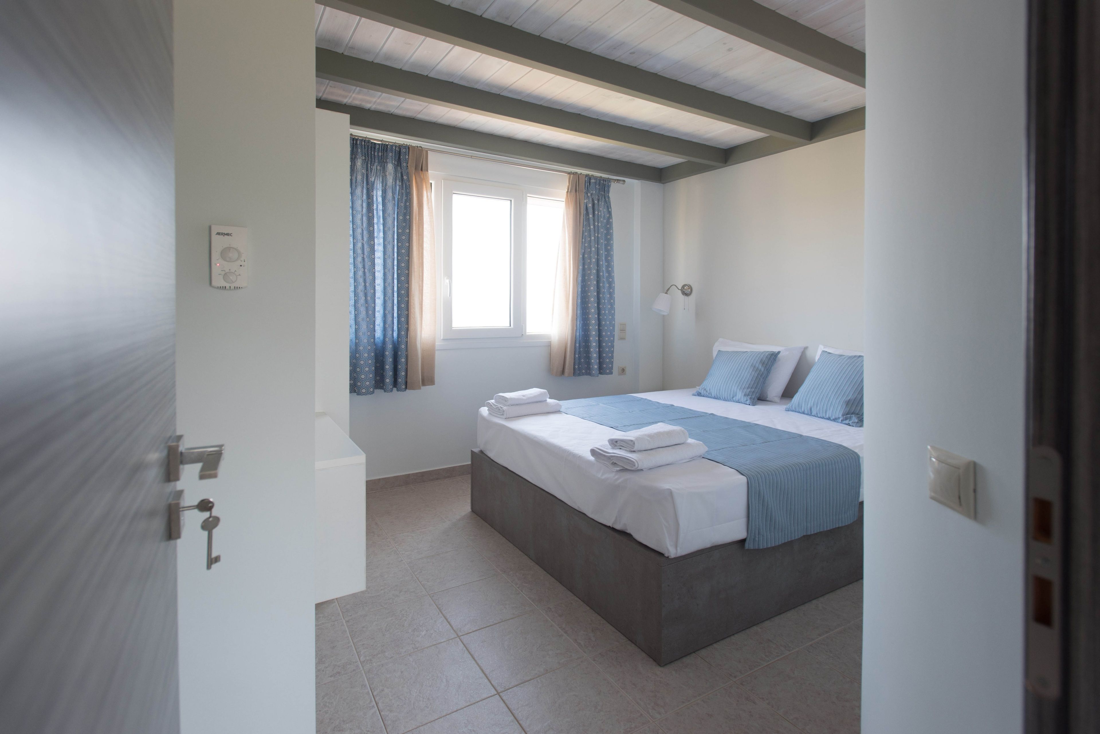 Une chambre à coucher avec un lit, des rideaux, une fenêtre et un thermostat fixé au mur.