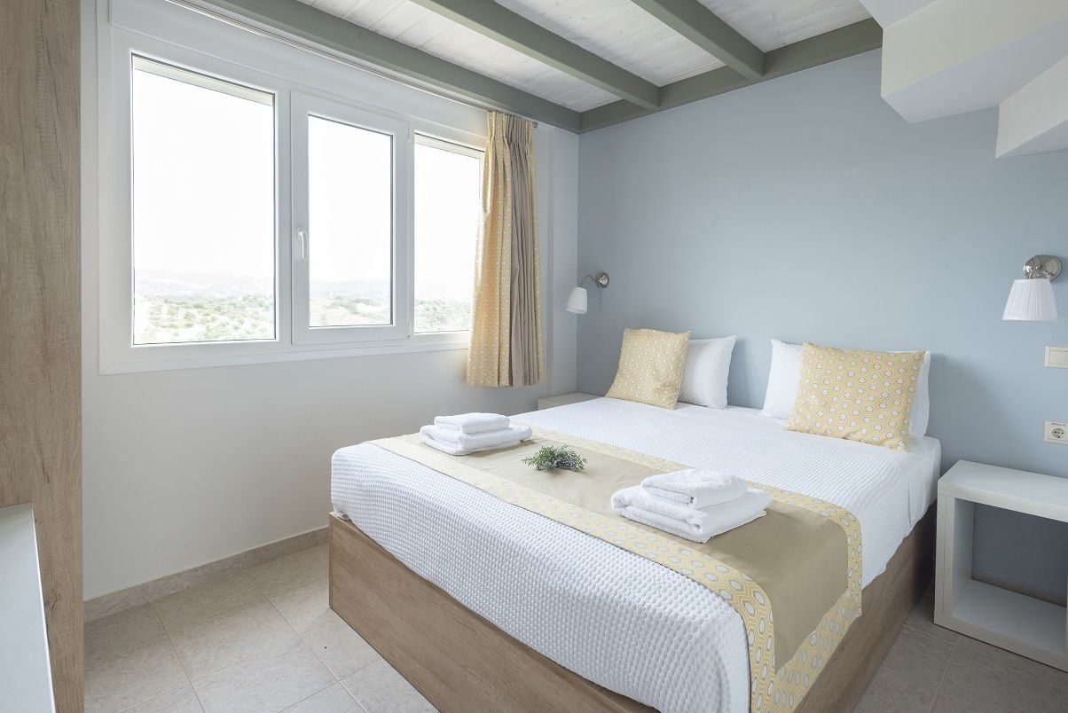 A bedroom with a large bed, two bedside tables, a window with curtains, and a view of the outdoors.