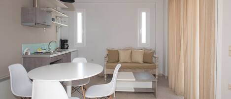 A modern kitchen with white cabinets, a round dining table with four chairs, and a beige sofa in the living area.