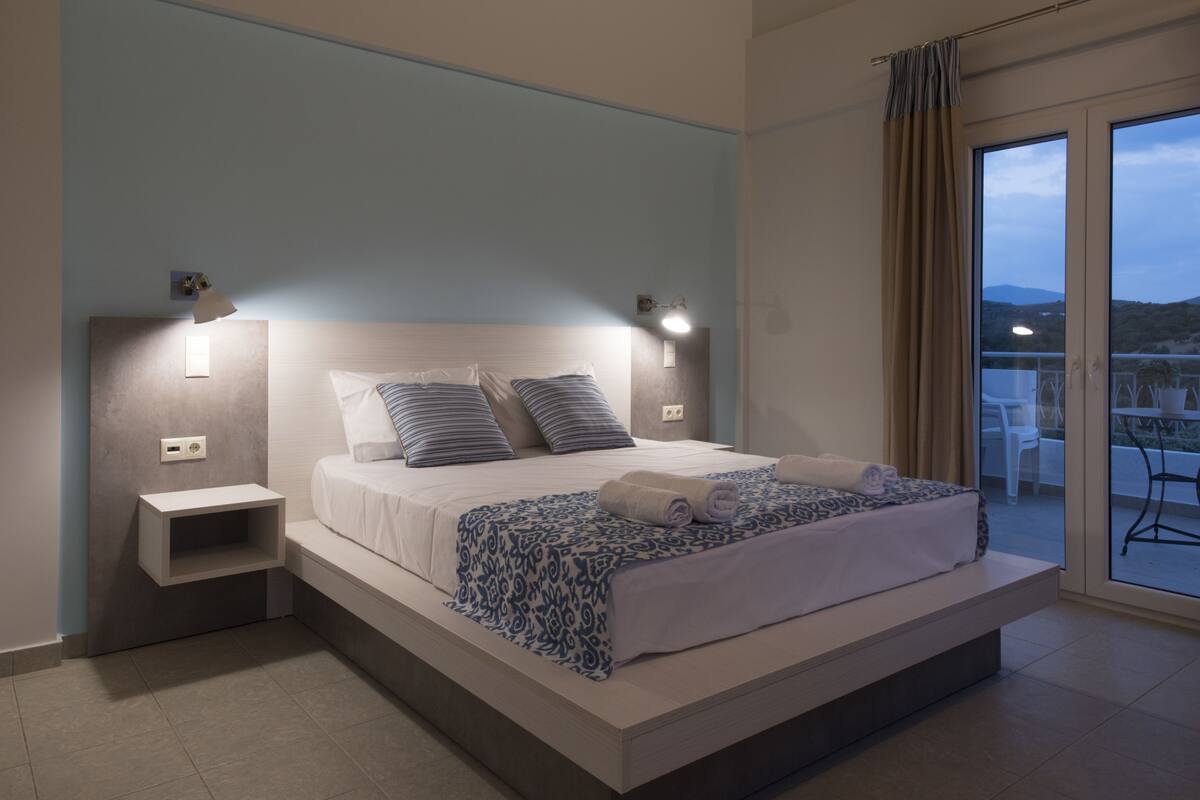 Quarto moderno com uma cama grande, mesas de cabeceira e vista para o exterior.