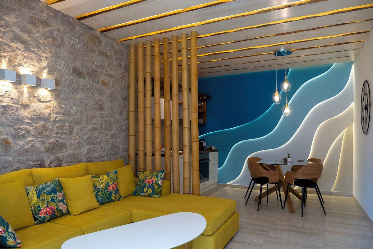 Uma sala de estar moderna com um sofá amarelo, uma mesa de centro branca e uma área de jantar com cadeiras de madeira.