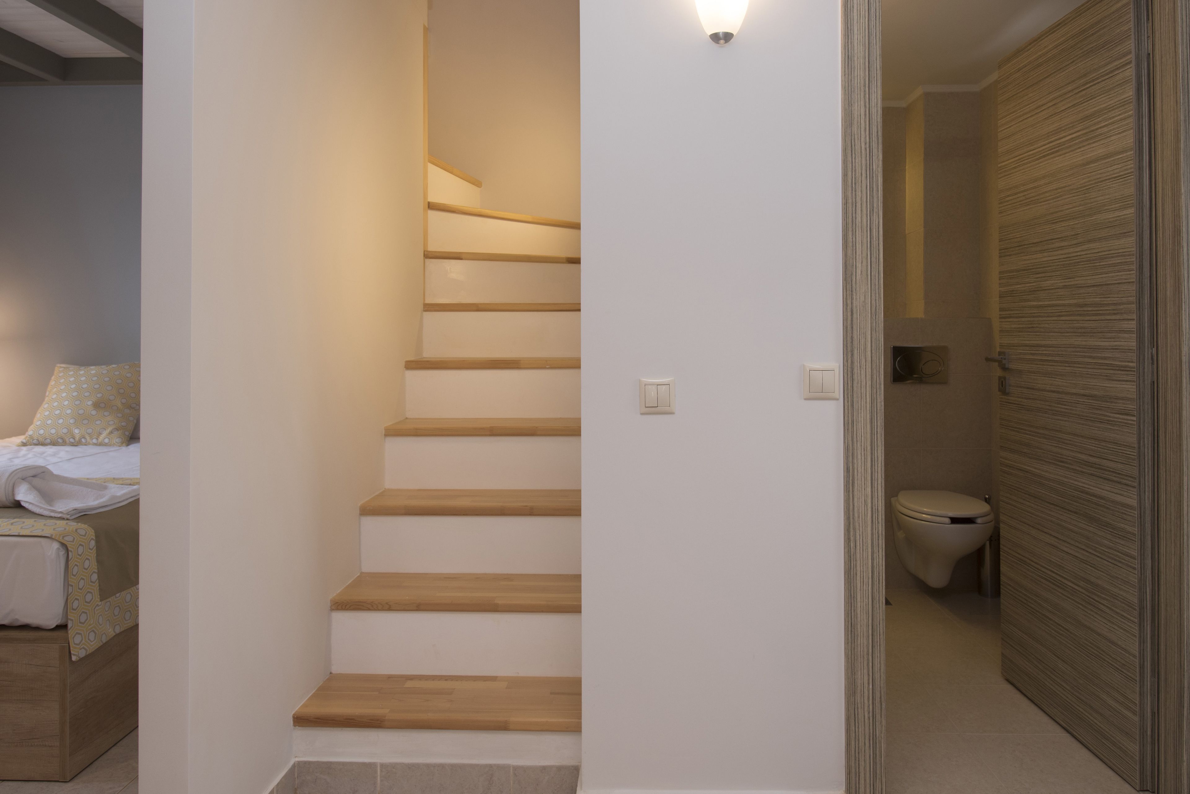 En trappe fører op til et badeværelse med toilet og en seng med et mønstret sengetæppe.