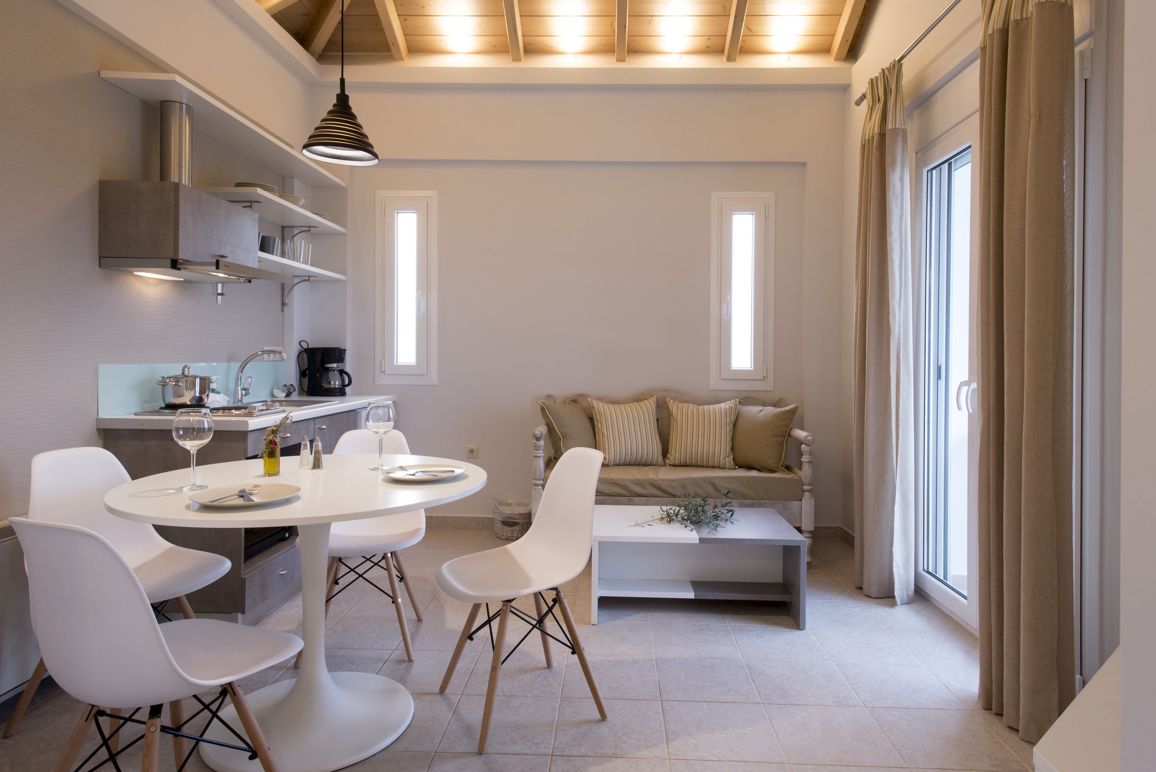 A modern kitchen with white cabinetry, a dining table with chairs, and a sofa in the living area.