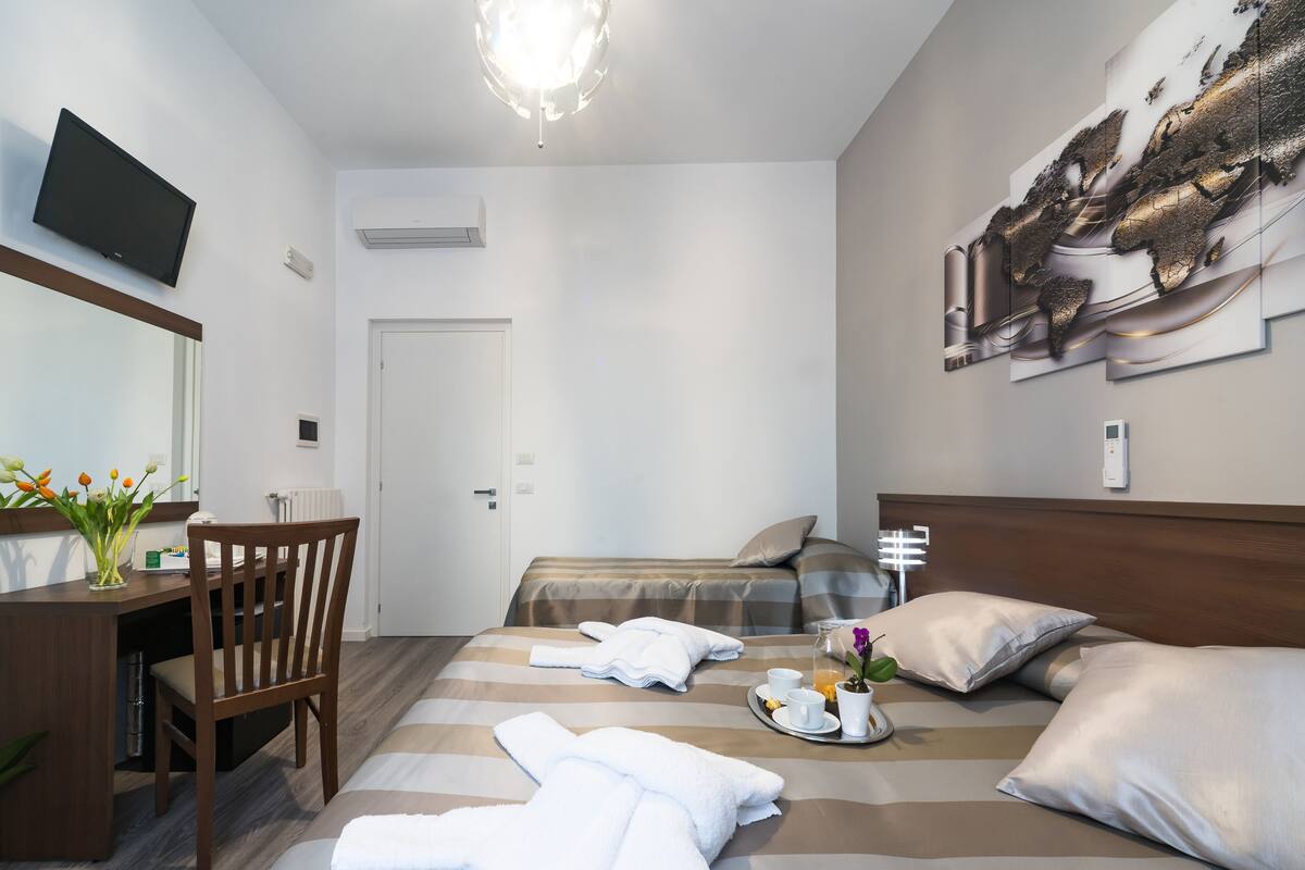 A hotel room with a bed, a desk with a chair, a TV, and a wall-mounted artwork.