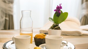Uma bandeja com duas chávenas brancas, um muffin, um copo de chá e uma pequena planta de orquídea sobre uma mesa.