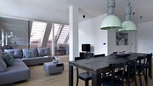 A modern living space with a sofa, dining table, and chairs, a television, and artwork on the walls. - Hotel Maribor, City apartments (Maribor)