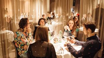 Un groupe de personnes est assis à une table recouverte d’une nappe blanche, et des rideaux les entourent.