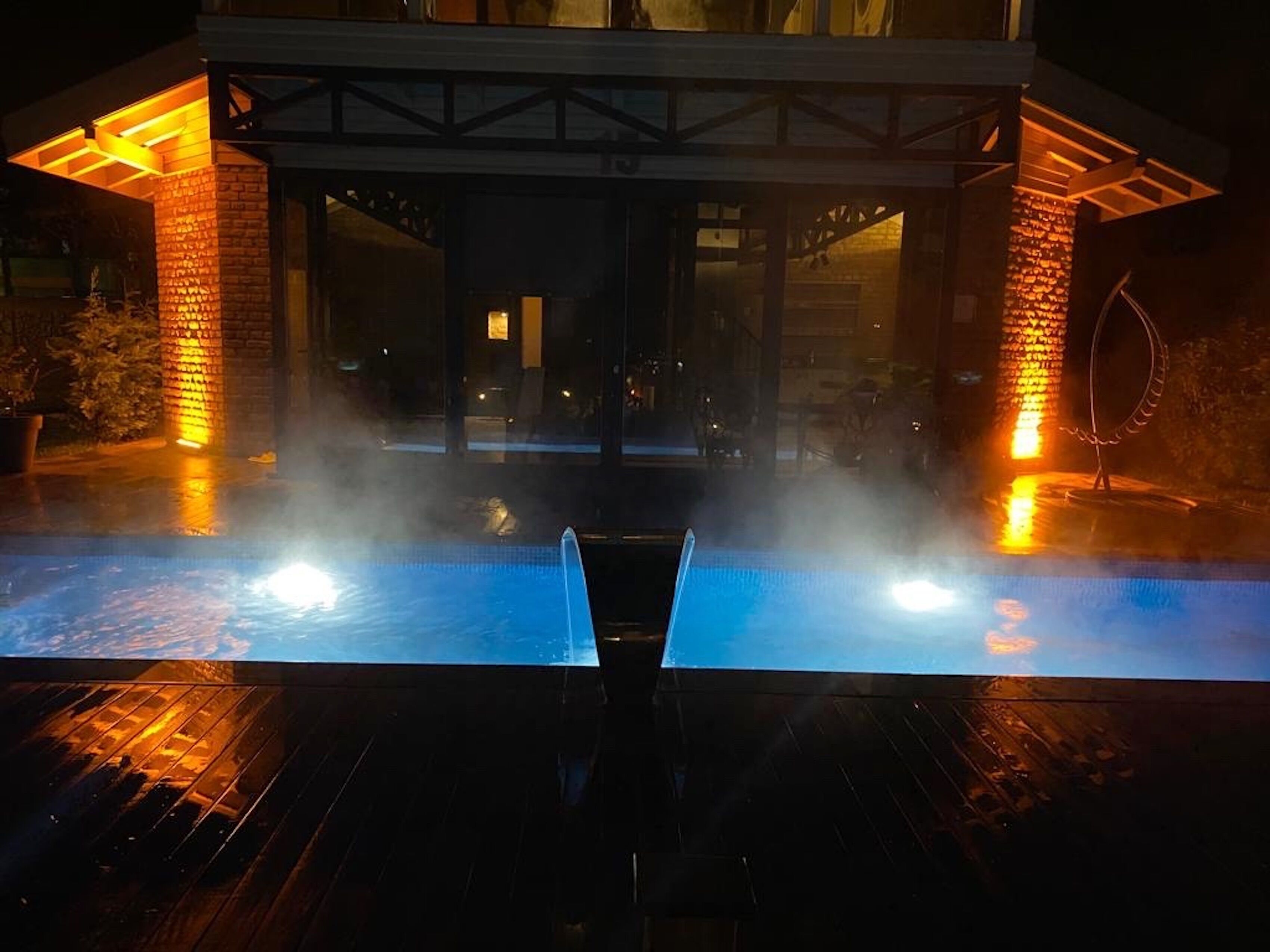 Un espace avec un bain à remous, doté d’une terrasse en bois, de piliers en briques et de portes vitrées donnant sur un espace abrité.