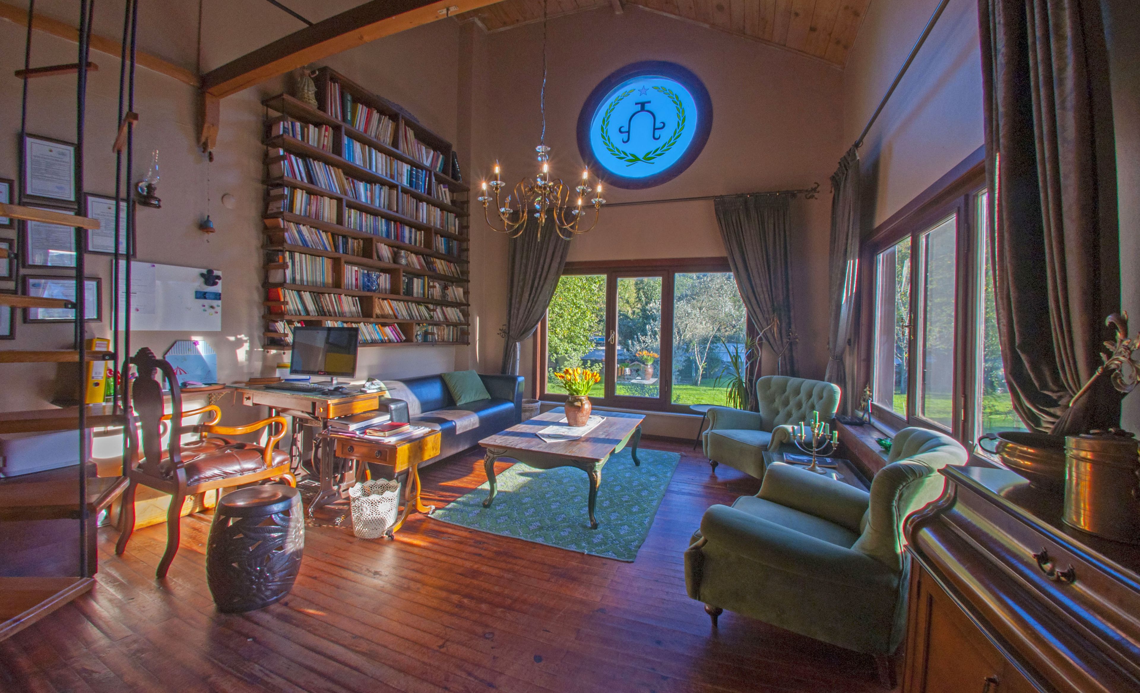 A spacious living room with a large bookshelf, a comfortable seating area, and a view of the outdoors through large windows.