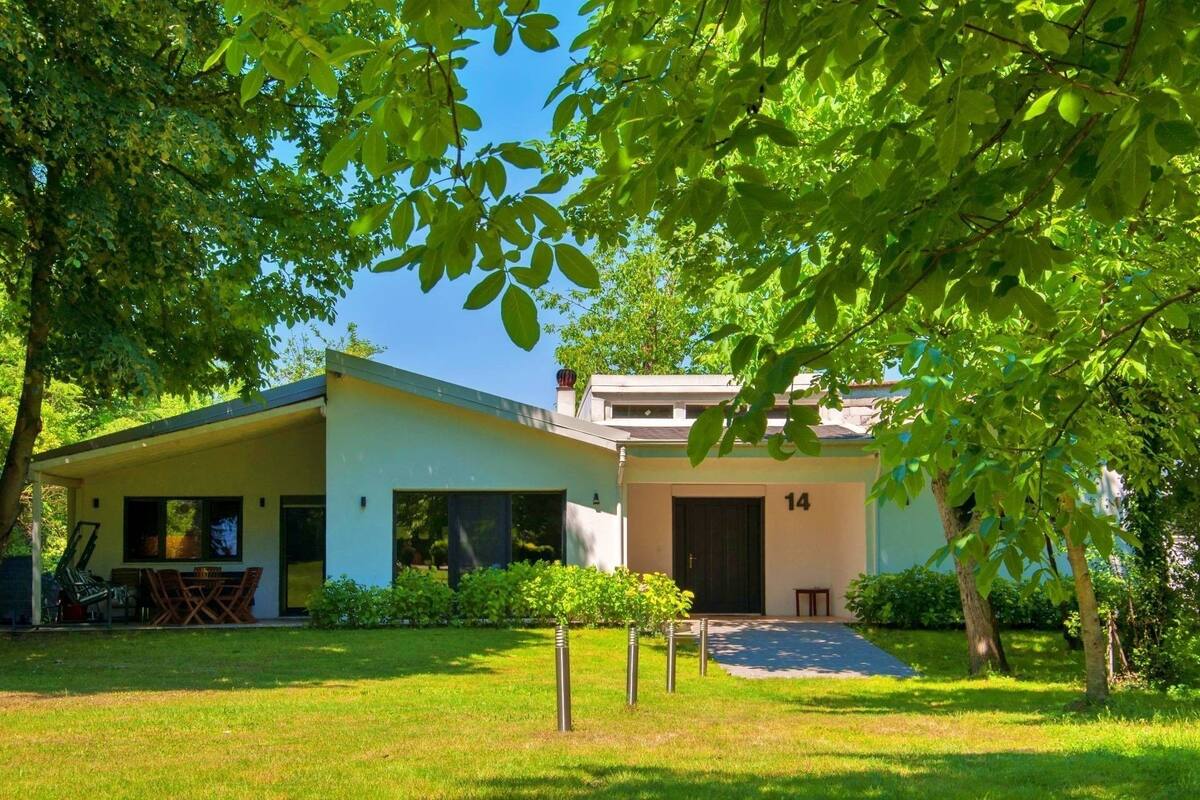 Een modern huis met twee verdiepingen, een plat dak, een overdekte patio en een bord met nummer 14.