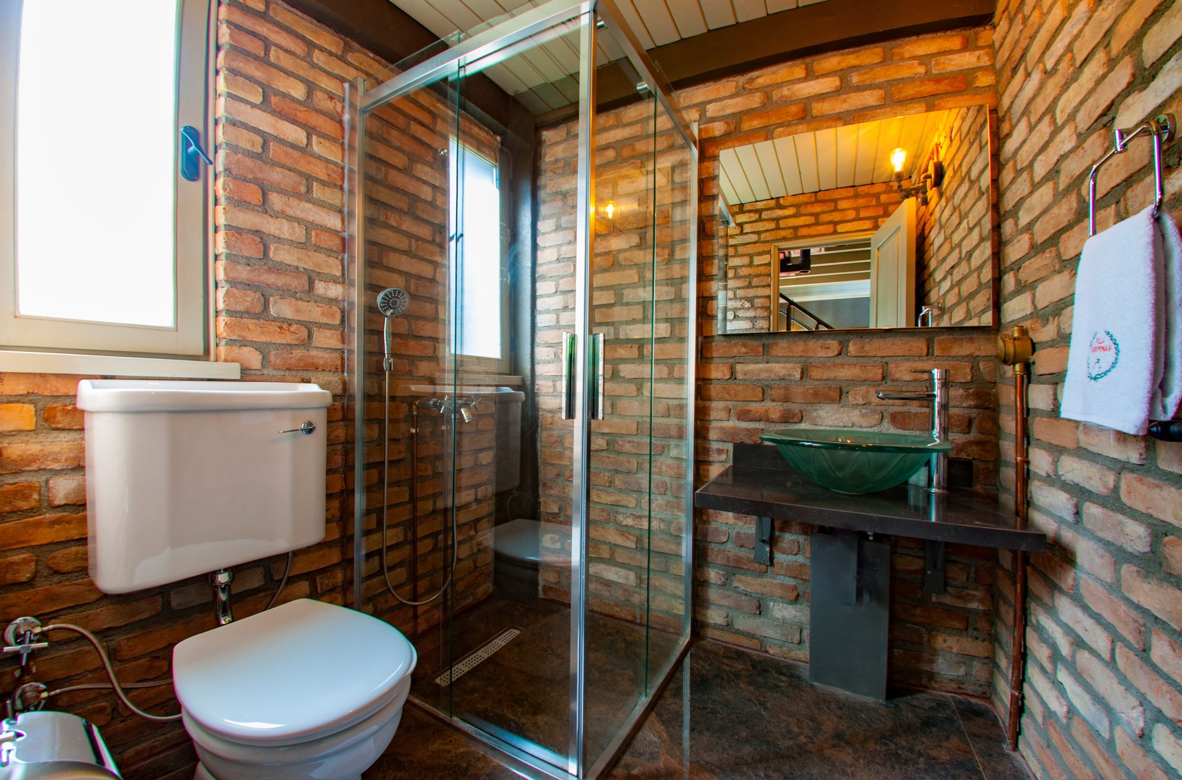 Een badkamer met een douchecabine van glas, een wit toilet en een bakstenen muur.