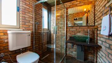 Een badkamer met een douchecabine van glas, een wit toilet en een bakstenen muur.