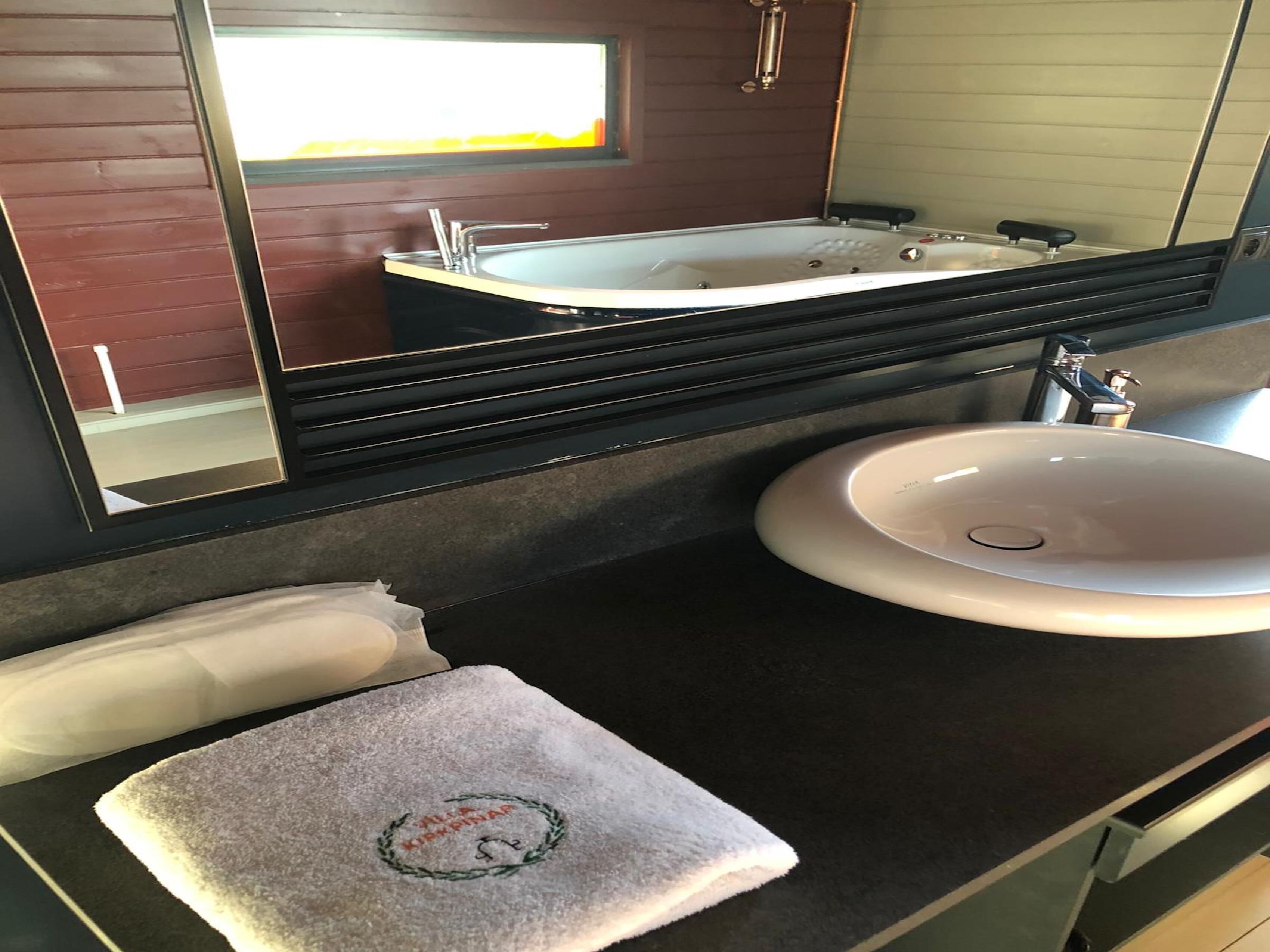 Un baño con un espejo grande, una bañera, un lavabo y una toalla con un logotipo.
