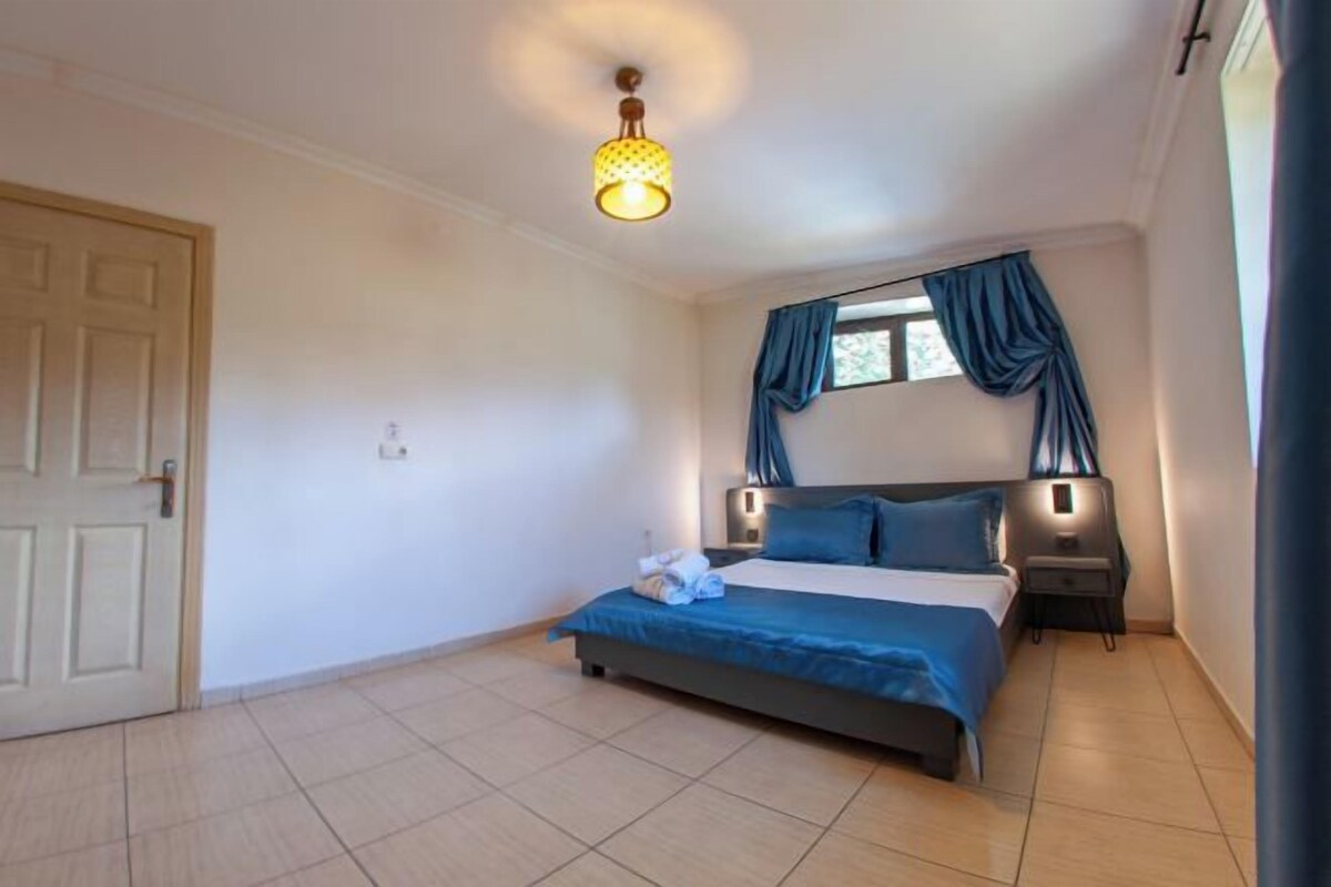 Un dormitorio con cama, mesita de noche, lámpara, ventana con cortinas y puerta.