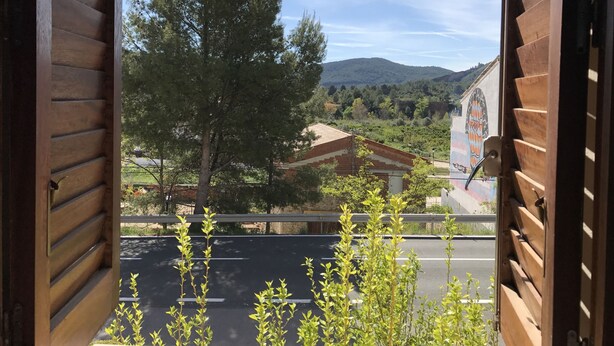 A view from a wooden-framed window overlooking a road, a tree, and a building with a mural.