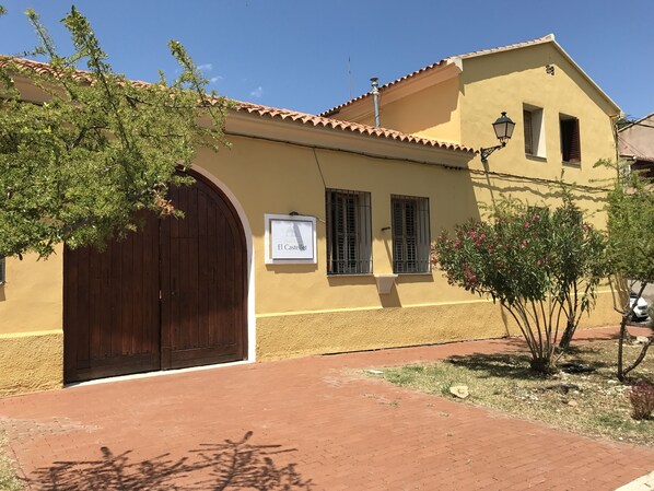 A building with a large wooden door, a sign reading "El Castillo", and a small window with shutters.