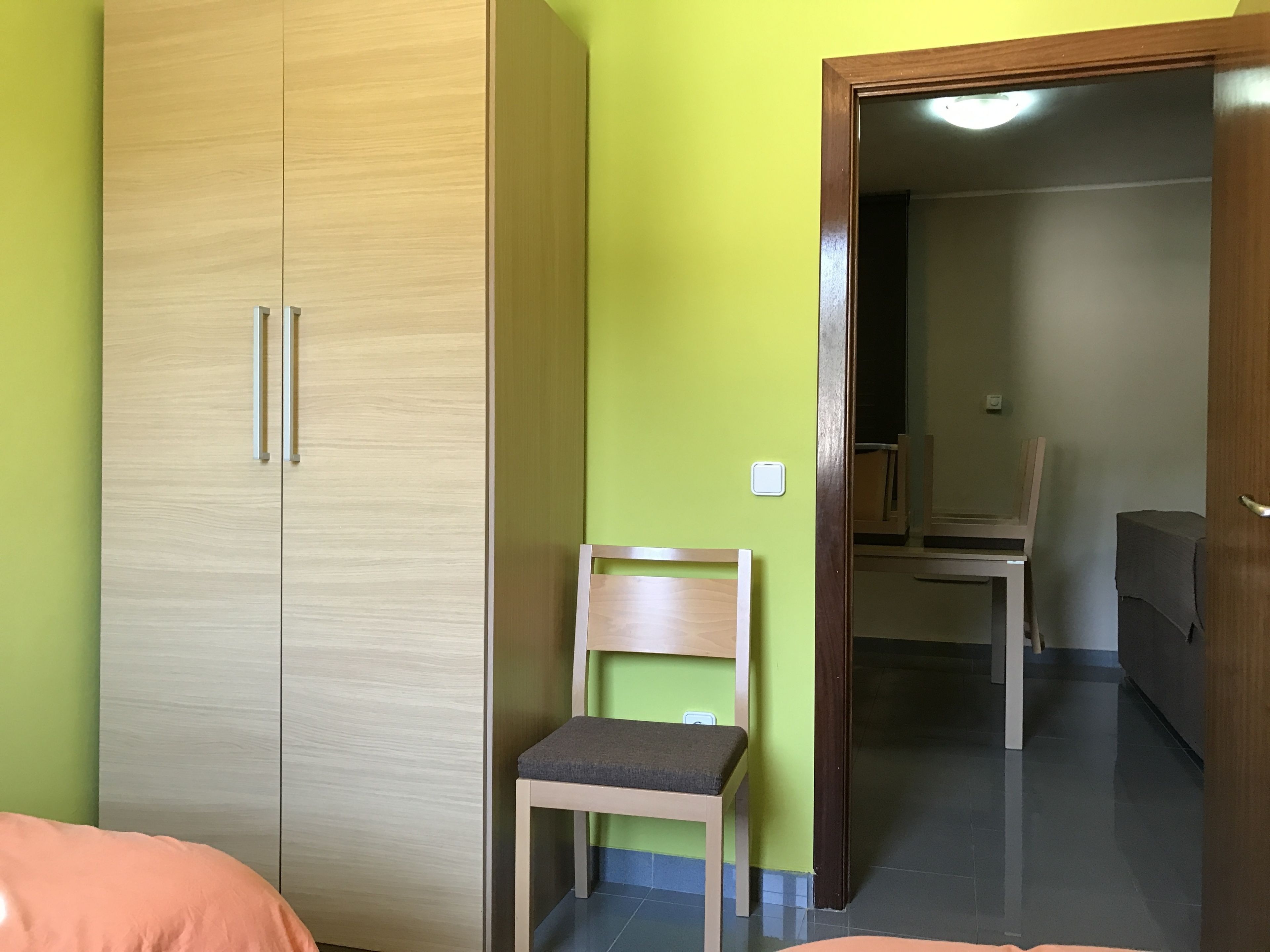 A room with a wardrobe, a chair, and a bed.