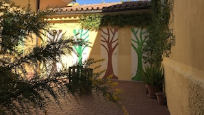 A courtyard with a tiled roof, potted plants, and a mural of trees.
