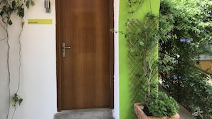 A wooden door with a metal handle, a small sign reading "privado", and a green wall with climbing plants and a potted plant.