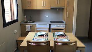 A compact kitchen with wooden cabinets, a built-in oven, and a stove. There is a dining table set with plates and cutlery.