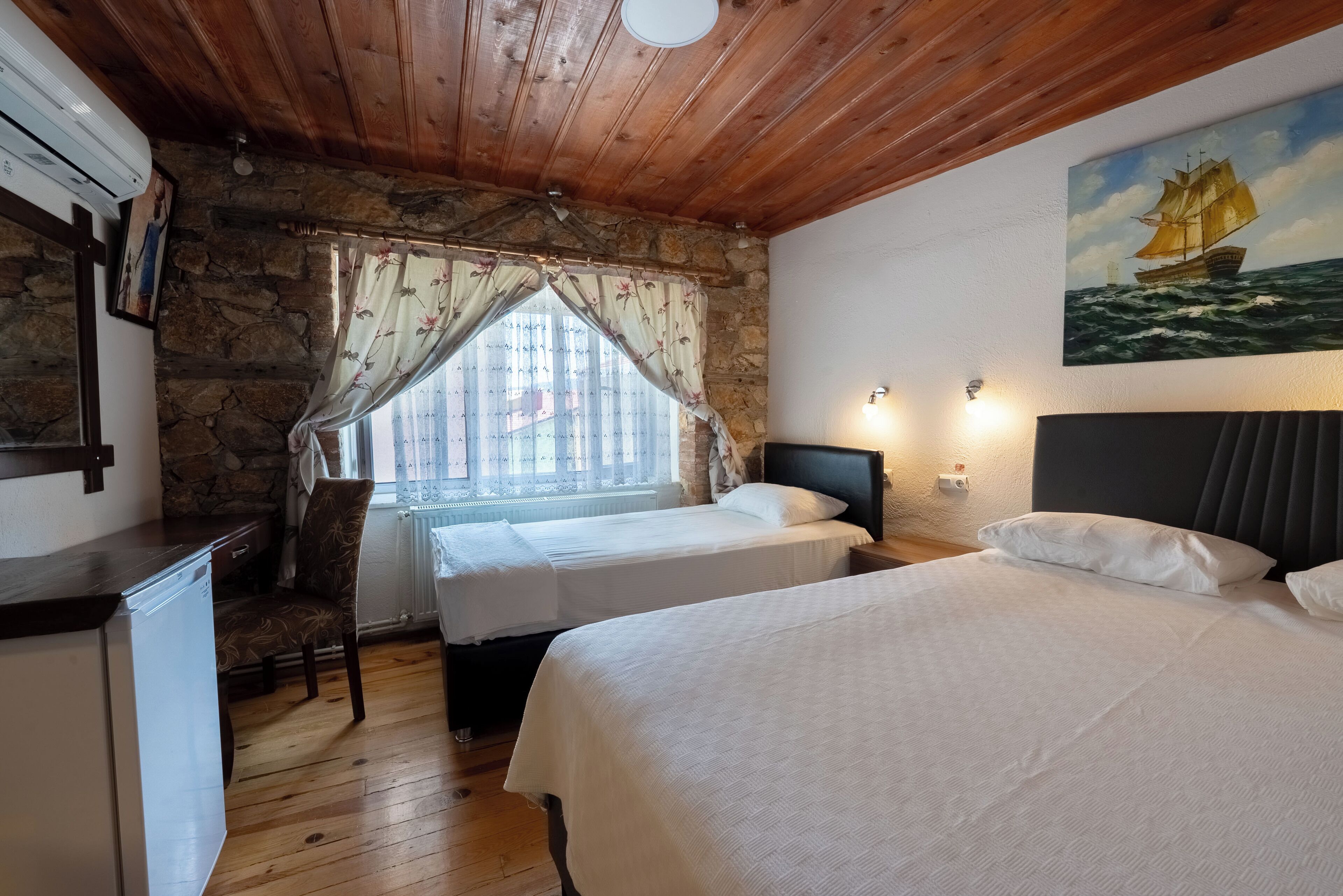 Una habitación acogedora con dos camas, una pared de piedra, techo de madera y un cuadro de un velero.