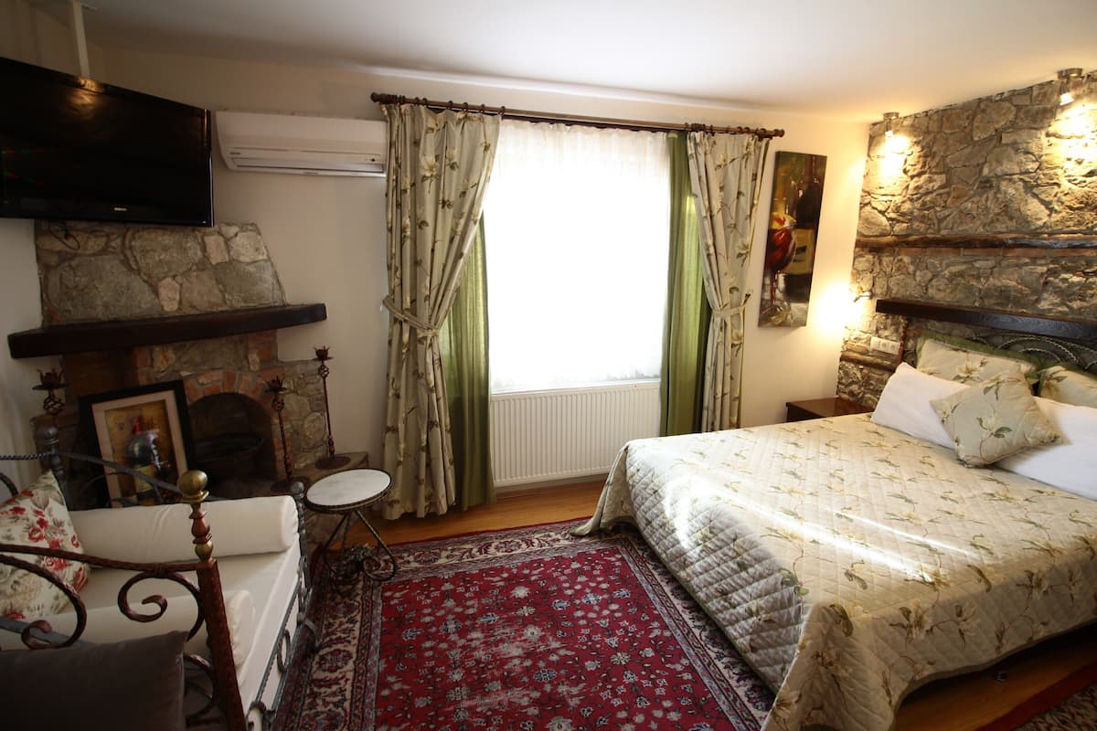 Un dormitorio con chimenea de piedra, una cama con ropa de cama floral, alfombra roja estampada y un televisor montado en la pared.