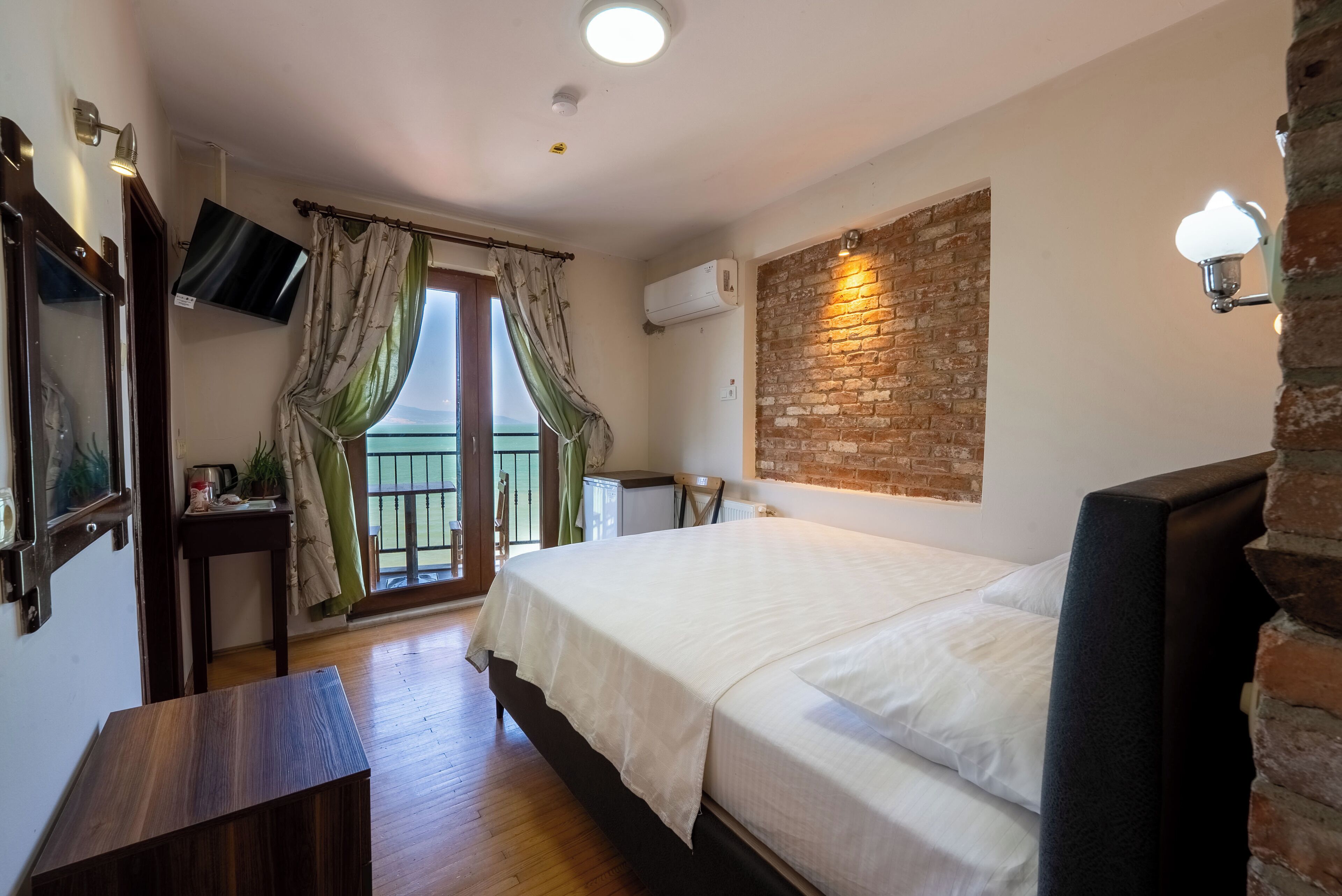 Un dormitorio con cama, escritorio, televisor y balcón con cortinas.