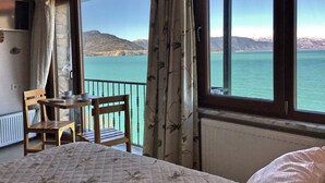 A room with a bed, a table with chairs, and a view of a lake and mountains through large windows. - Fulya Pension (Egirdir)