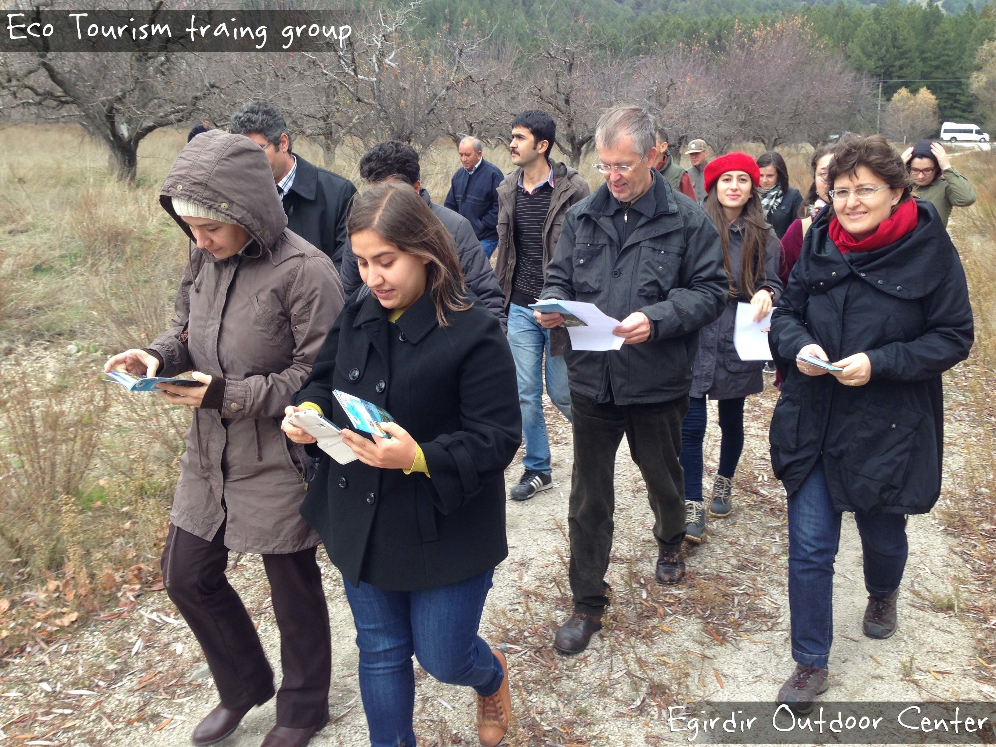 A group of people walking outdoors, some holding maps or papers, likely on an eco-tourism trip.