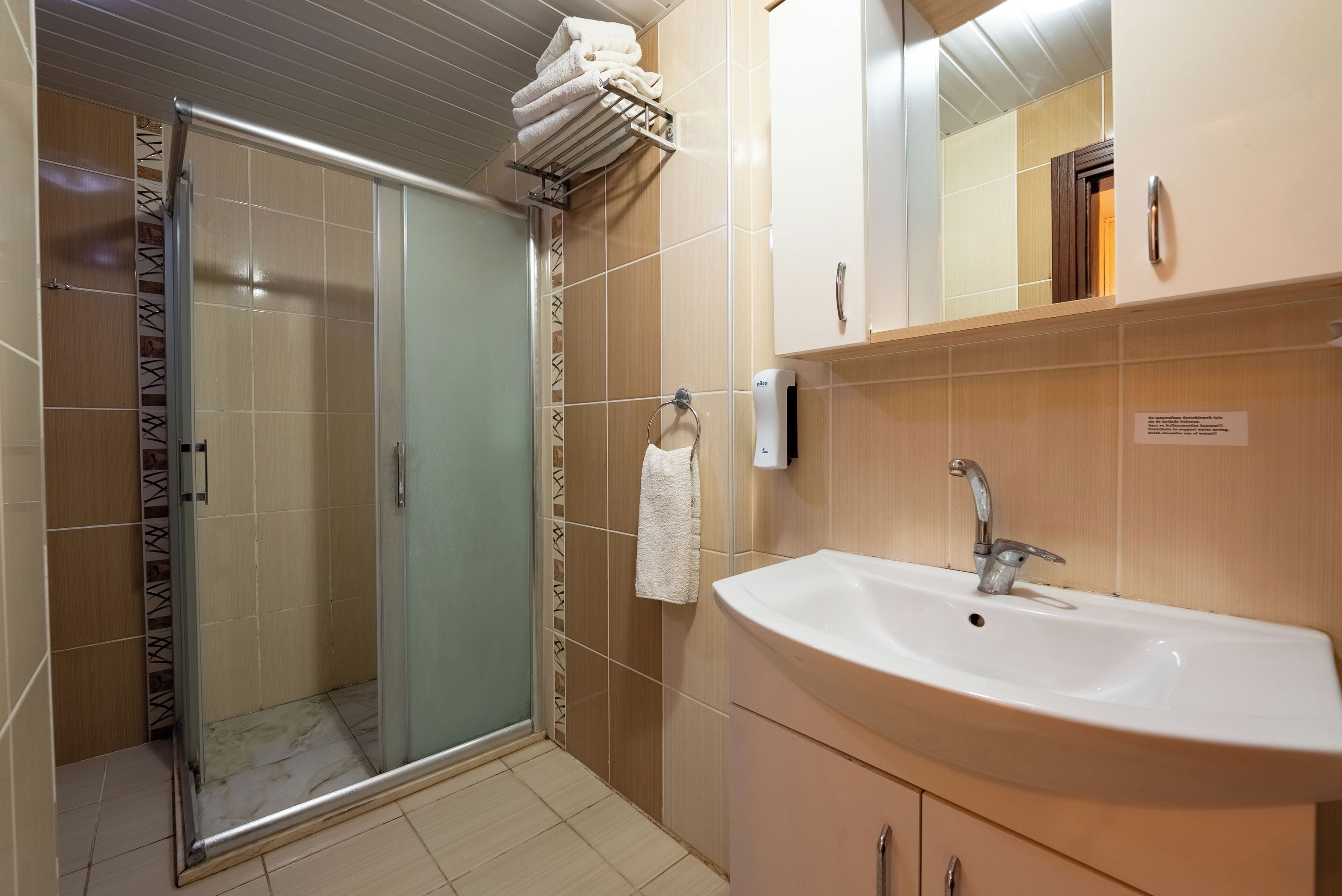 Een badkamer met een douche met glazen wand, een wastafel met spiegel en een handdoekrek.