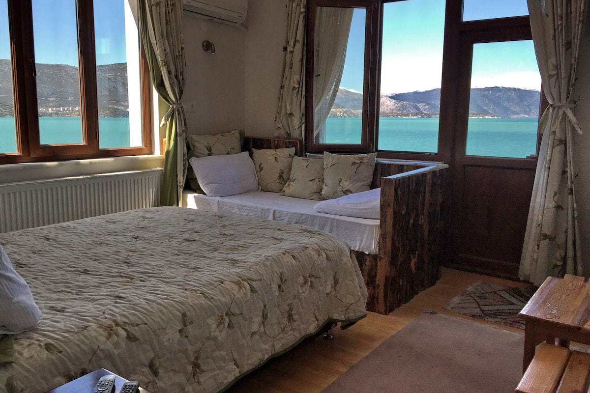 Un dormitorio con cama, un banco de madera y vista a un lago y montañas.