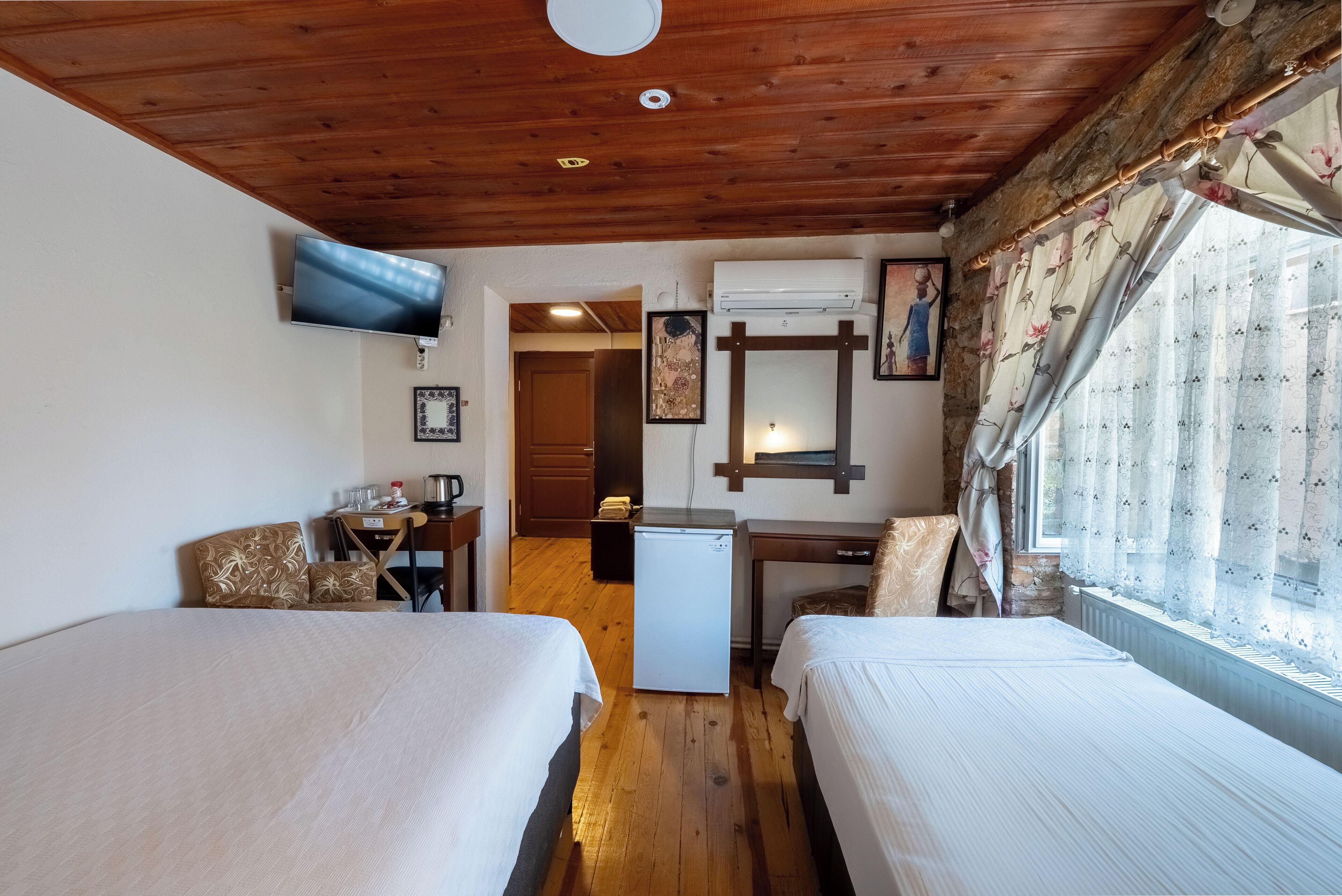 A room with two beds, a TV, a desk, a refrigerator, and a window with curtains.